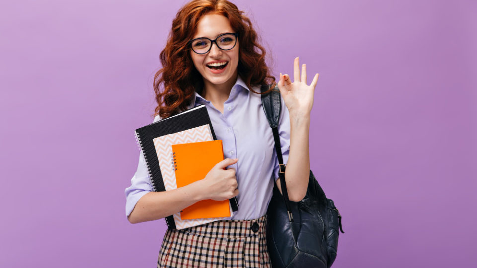 red-haired-lady-eyeglasses-holds-books-shows-ok-sign
